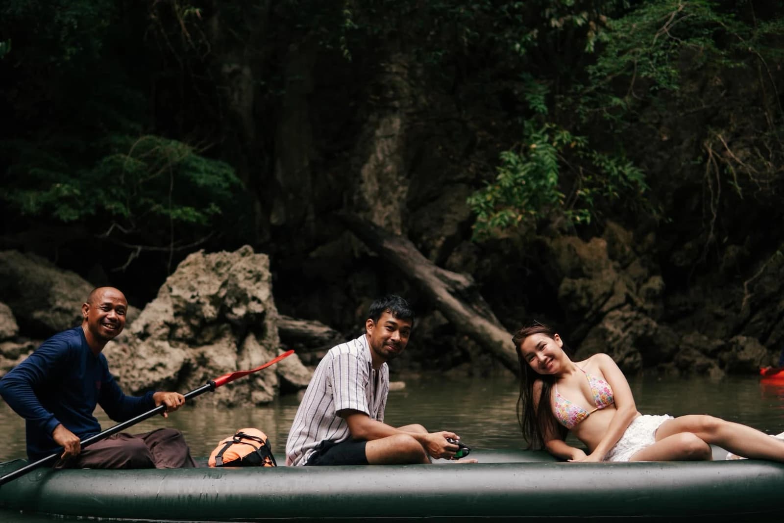 Guide and guests in a canoe beside a shaded forested rock wall