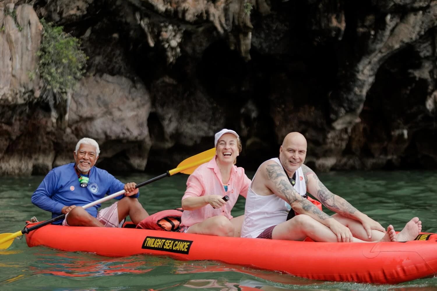 A guide and two guests seated in a red canoe beside a cave entrance