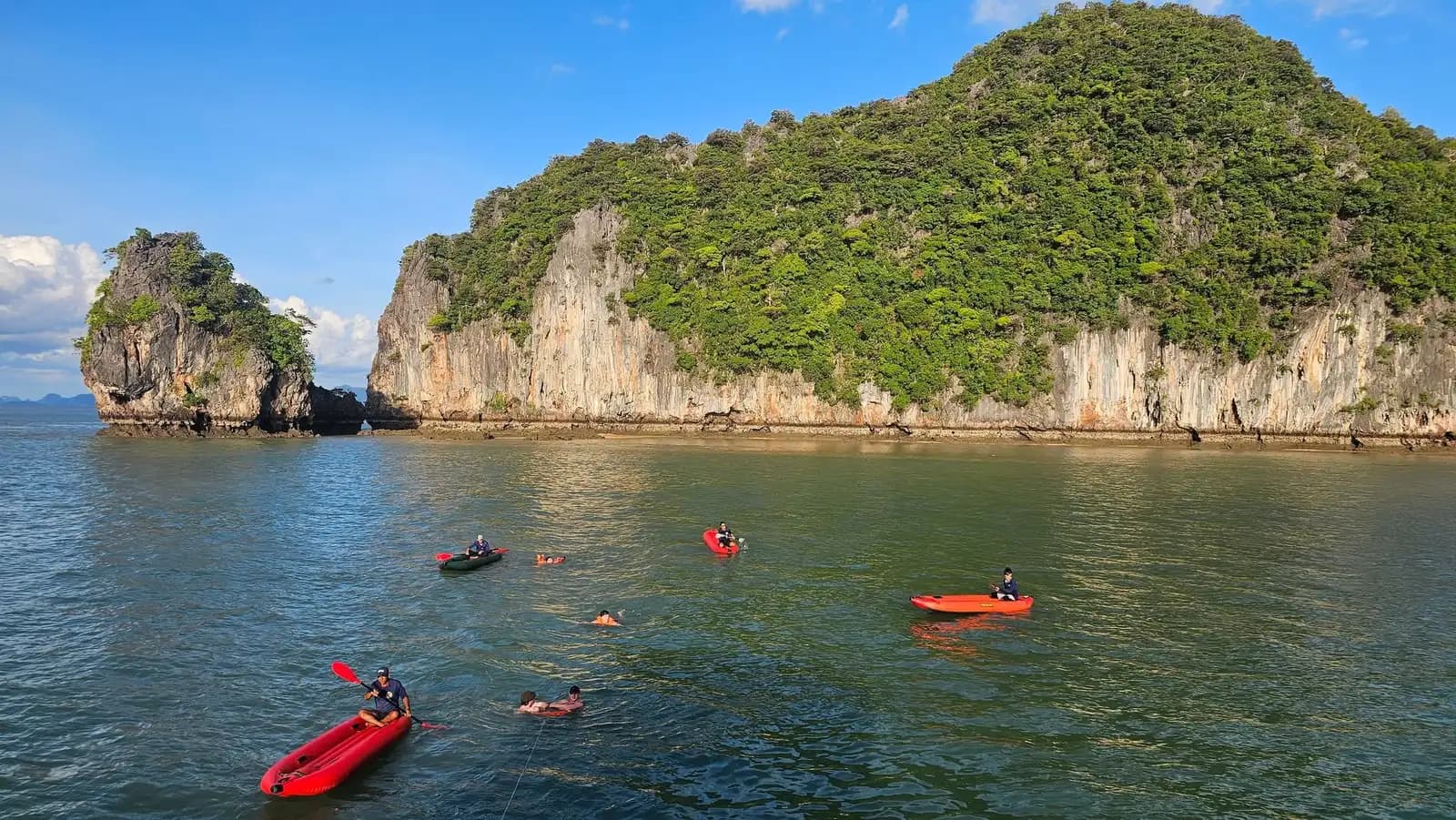 Red canoes approaching a wooded limestone shoreline