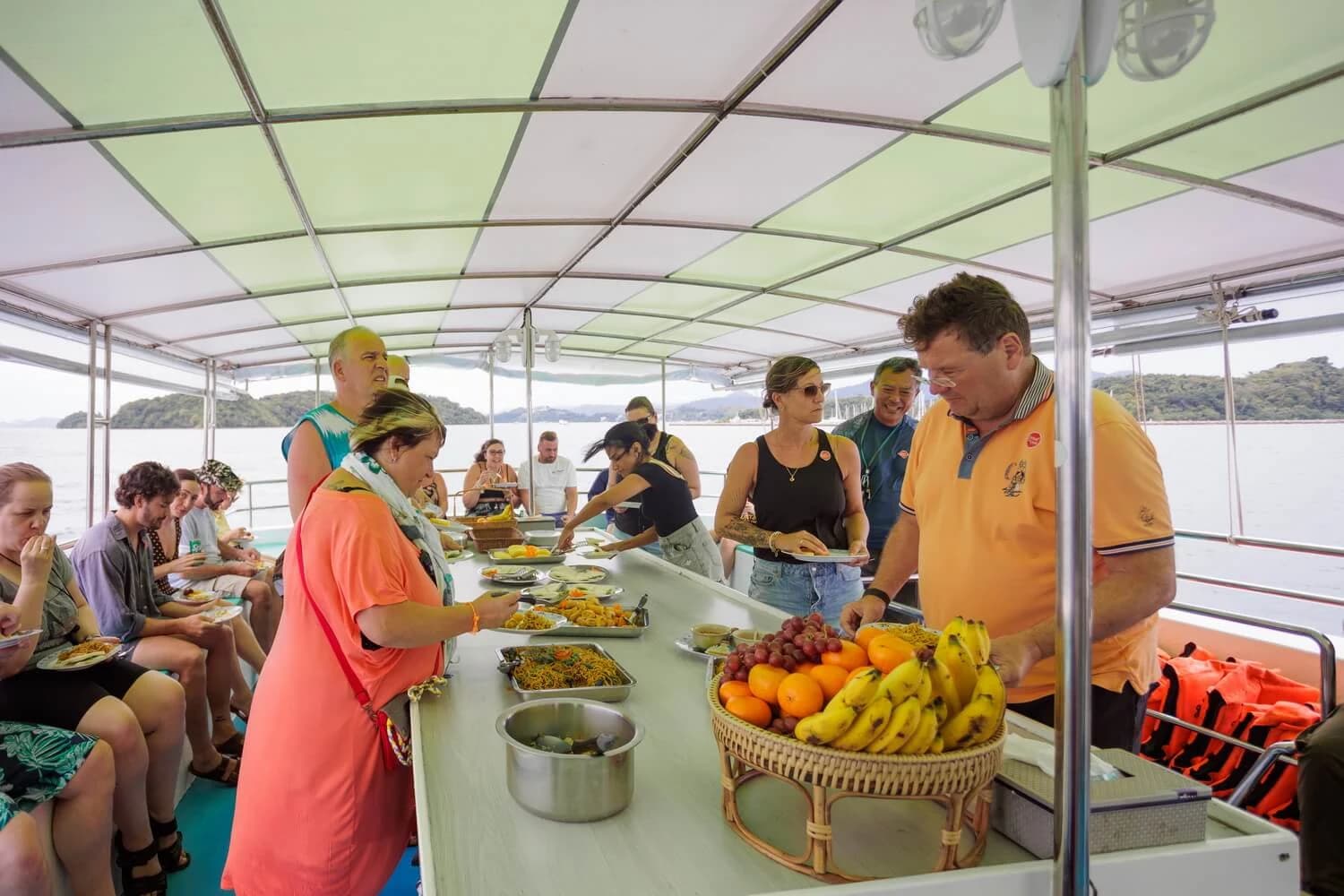 Guests choosing food and fruit from a buffet aboard the tour boat